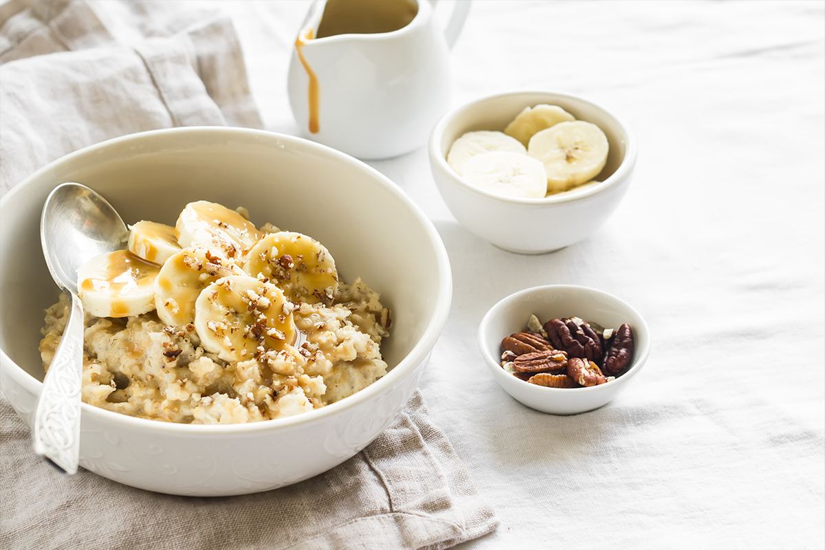 oatmeal with banana, caramel sauce and pecans in a white bowl on a light surface, a delicious and healthy Breakfast